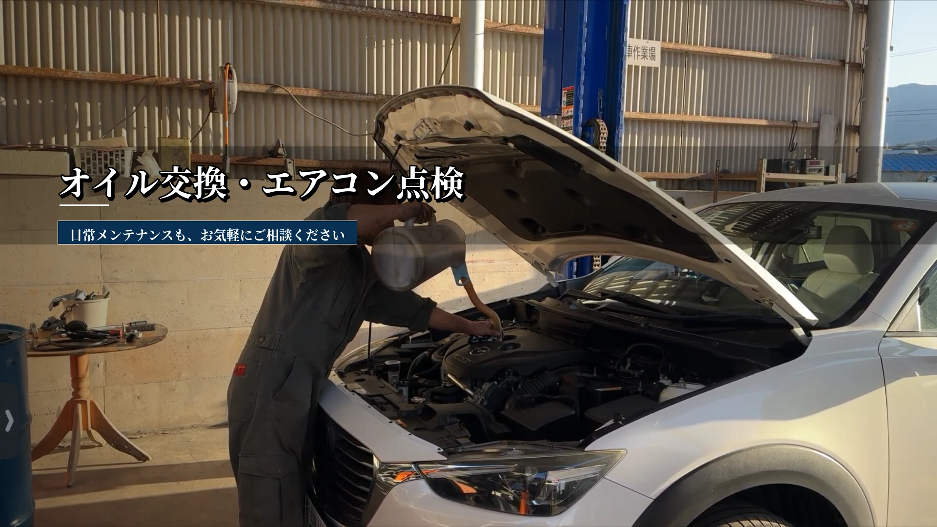 整備工場で整備士がボンネットを開けた車にオイルを補充している、オイル交換・エアコン点検の案内画像