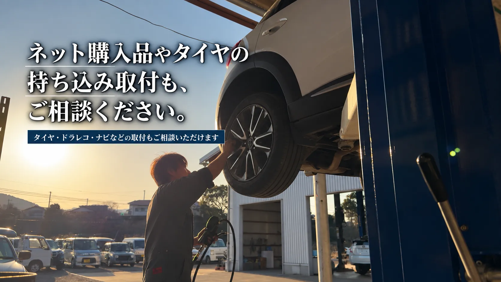 夕暮れの整備工場で、リフトアップされた車のタイヤまわりを整備士が確認しているタイヤ・部品の持ち込み取付案内画像